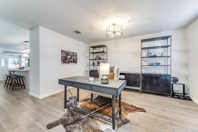 home office with a textured ceiling, wood finished floors, visible vents, and baseboards