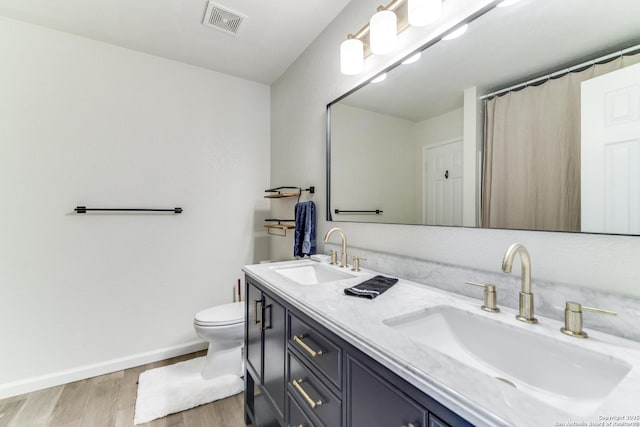 full bath with toilet, visible vents, a sink, and wood finished floors