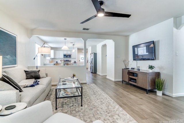 living room with arched walkways, visible vents, light wood-style floors, ceiling fan, and baseboards