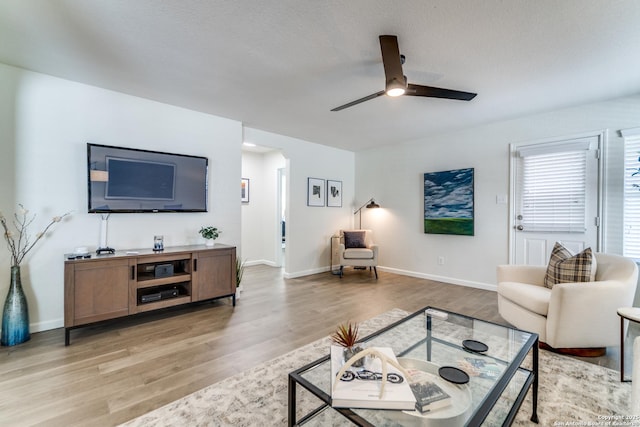 living area featuring arched walkways, a textured ceiling, a ceiling fan, baseboards, and light wood finished floors