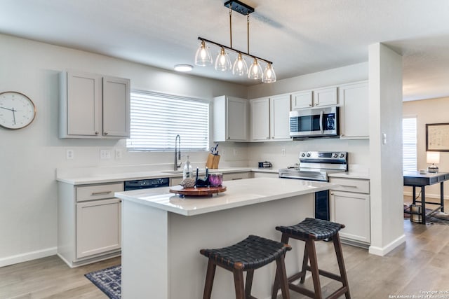 kitchen with stainless steel appliances, light countertops, light wood-style flooring, a sink, and a kitchen breakfast bar