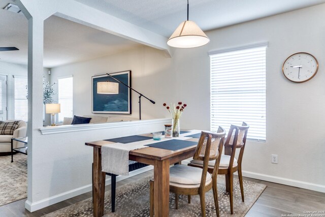 dining space featuring beamed ceiling, wood finished floors, and baseboards