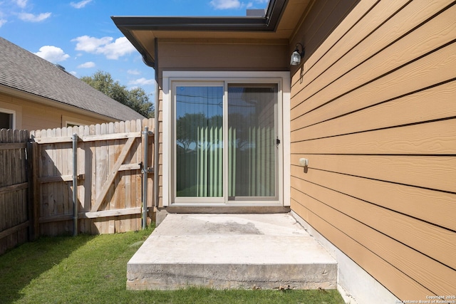 view of exterior entry featuring a gate, a lawn, and fence
