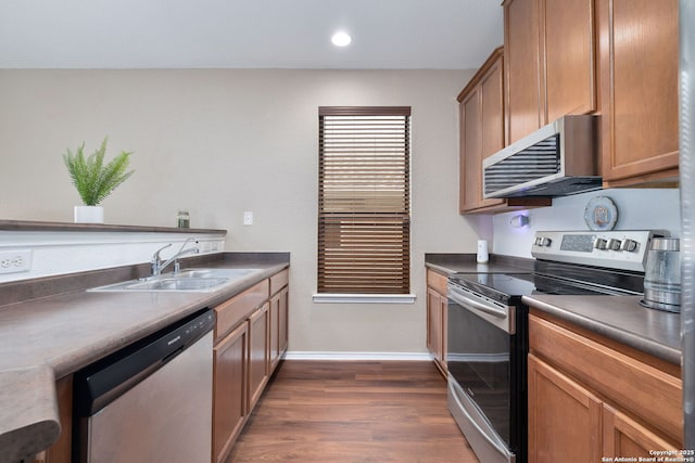 kitchen with dark countertops, a sink, baseboards, stainless steel appliances, and dark wood-style flooring