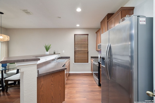 kitchen featuring dark countertops, visible vents, appliances with stainless steel finishes, a peninsula, and a sink