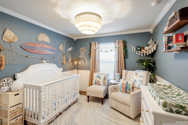 bedroom featuring a wainscoted wall, ornamental molding, a crib, and a textured ceiling