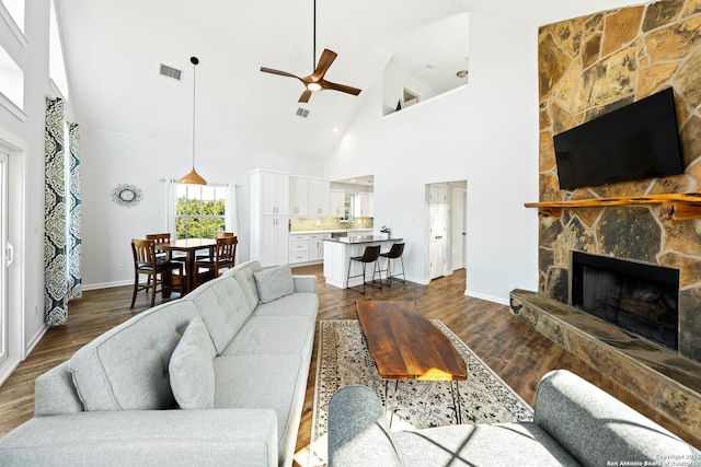 living room with a stone fireplace, dark wood finished floors, visible vents, and a ceiling fan