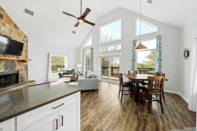 dining space with dark wood-style flooring, visible vents, a stone fireplace, and a healthy amount of sunlight