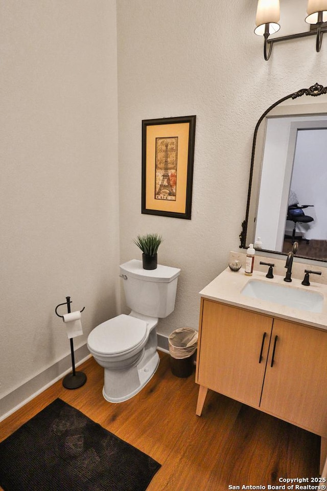 bathroom with toilet, wood finished floors, vanity, and baseboards