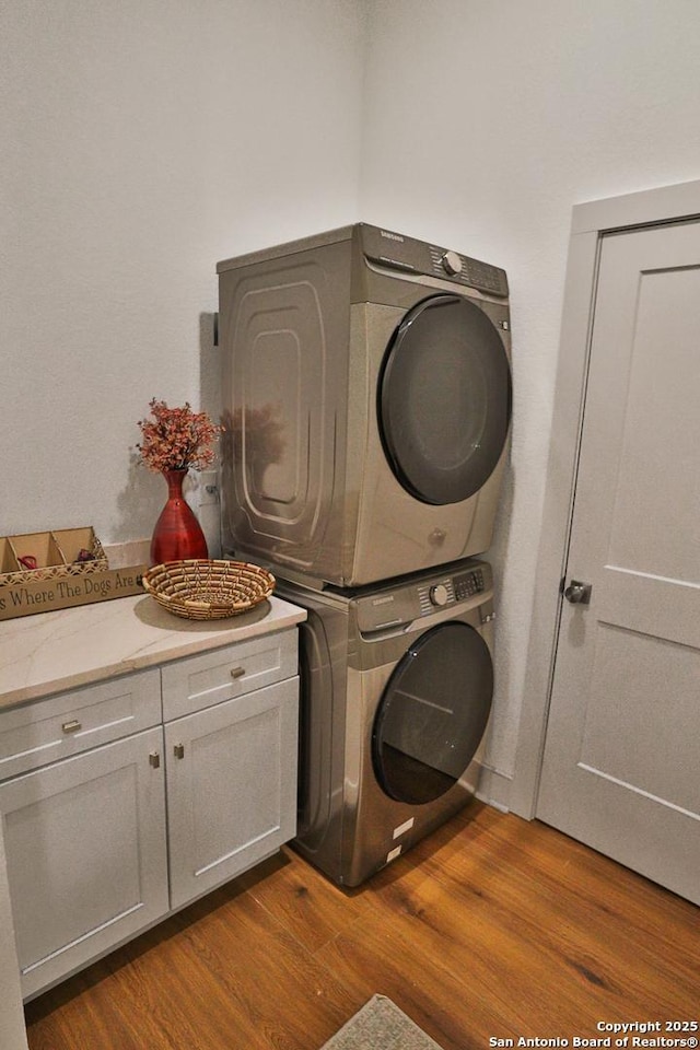 laundry room with stacked washer / dryer, dark wood finished floors, and cabinet space