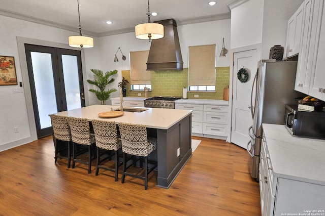 kitchen featuring wood finished floors, stainless steel appliances, crown molding, light countertops, and premium range hood