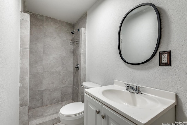 bathroom with tiled shower, a textured wall, vanity, and toilet