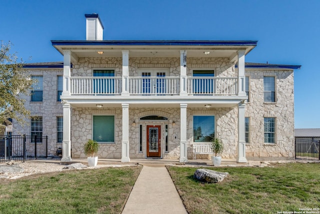 view of front of property featuring a porch, a balcony, fence, a chimney, and a front yard