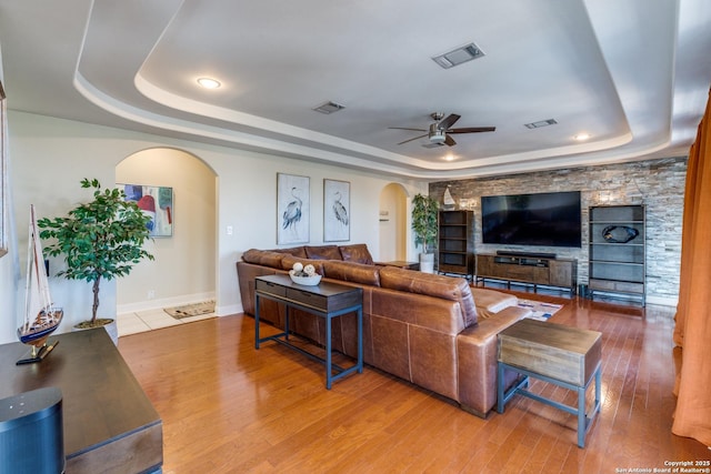 living area featuring a tray ceiling, visible vents, and arched walkways