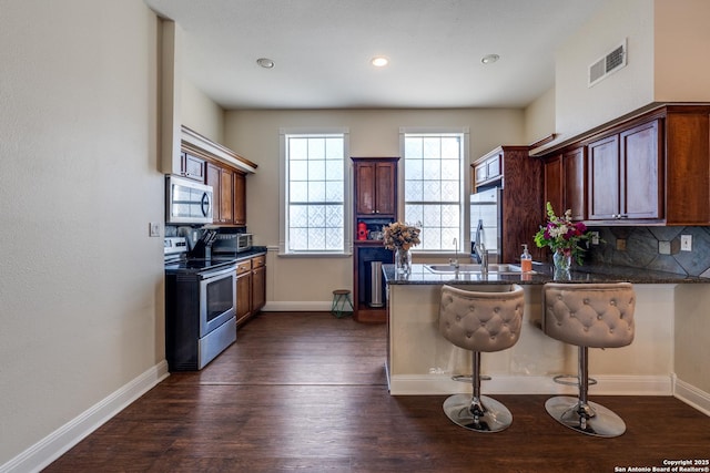 kitchen featuring stainless steel appliances, visible vents, decorative backsplash, dark wood-type flooring, and a peninsula