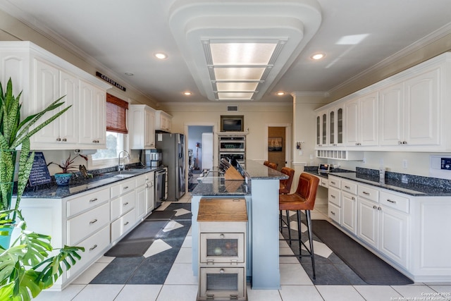 kitchen featuring white cabinets, appliances with stainless steel finishes, a kitchen breakfast bar, a center island, and a sink