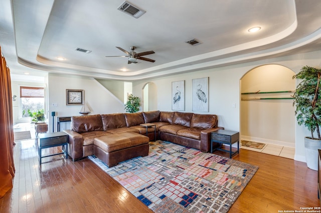 living area with hardwood / wood-style flooring, arched walkways, and a raised ceiling