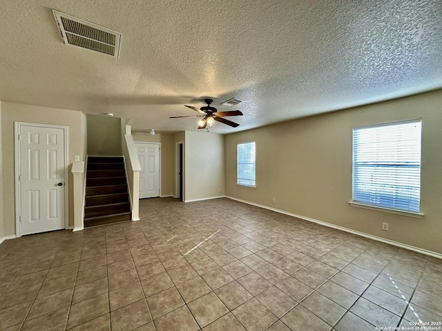 unfurnished room with visible vents, ceiling fan, tile patterned flooring, baseboards, and stairs