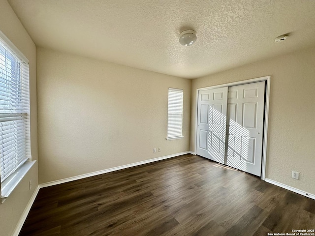 unfurnished bedroom featuring dark wood-style floors, a textured ceiling, and baseboards