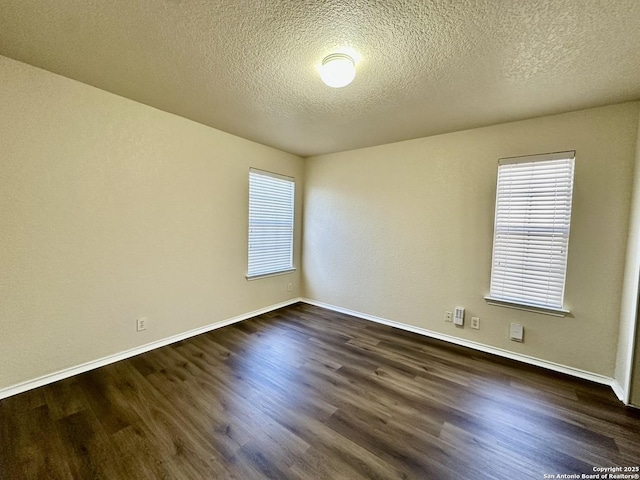 empty room with a textured ceiling, dark wood finished floors, and baseboards