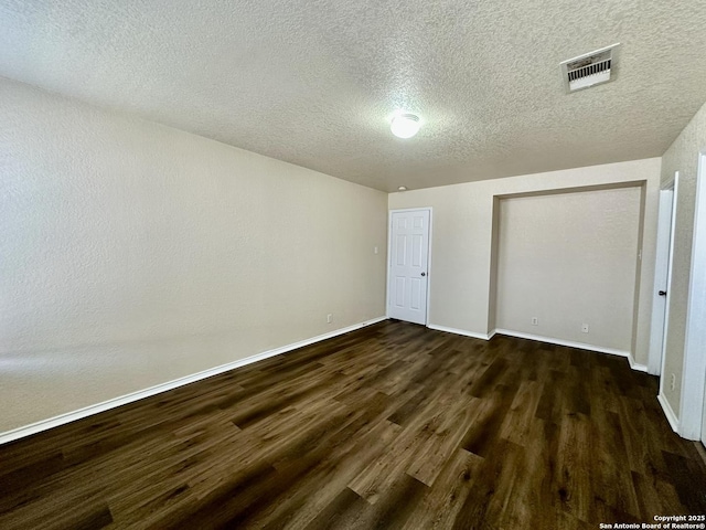 unfurnished bedroom with dark wood-type flooring, visible vents, a textured ceiling, and baseboards