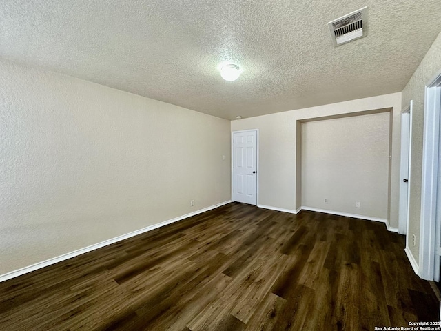 unfurnished bedroom featuring a textured ceiling, dark wood finished floors, visible vents, and baseboards