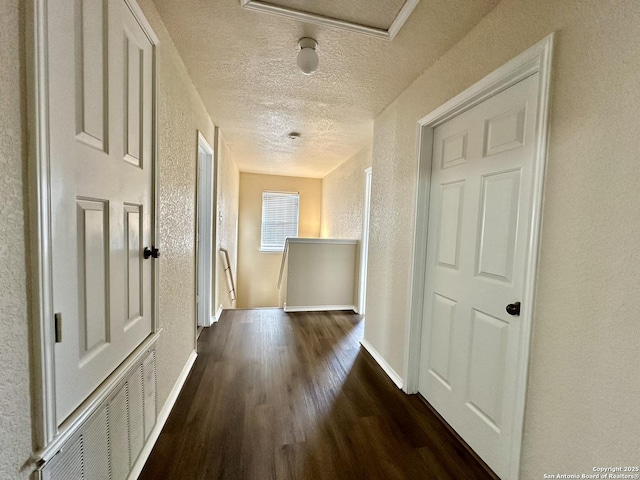 hallway with baseboards, dark wood finished floors, a textured wall, a textured ceiling, and an upstairs landing