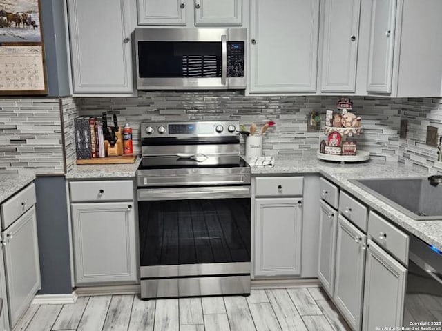 kitchen with wood tiled floor, appliances with stainless steel finishes, decorative backsplash, and light stone counters