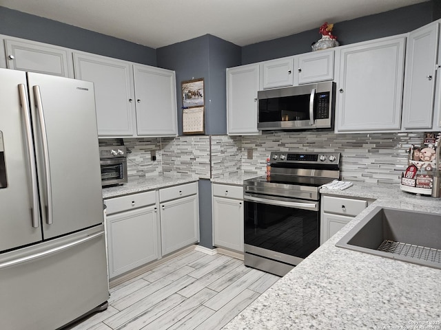 kitchen with stainless steel appliances, light wood-style flooring, white cabinetry, and decorative backsplash