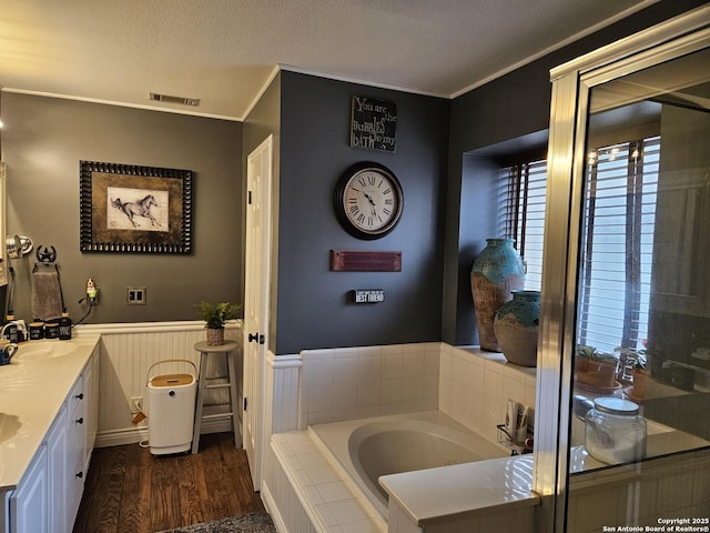 full bath featuring a wainscoted wall, ornamental molding, wood finished floors, a textured ceiling, and a sink