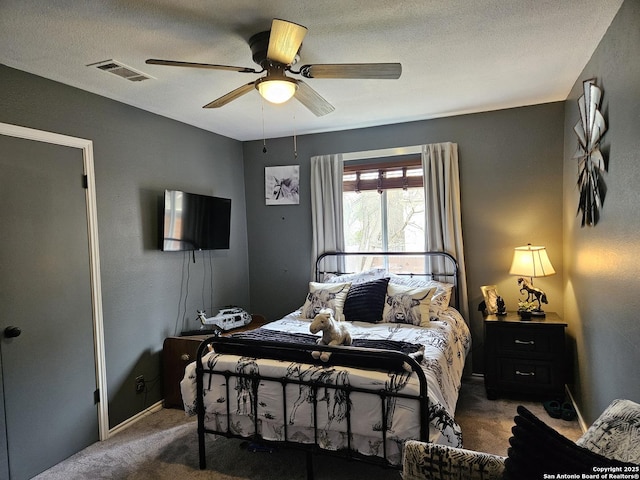 carpeted bedroom with a textured ceiling, baseboards, visible vents, and a ceiling fan