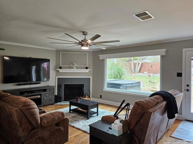 living room featuring light wood-style floors, visible vents, ornamental molding, and a tile fireplace