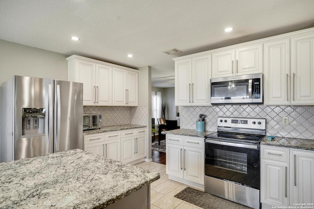 kitchen with visible vents, decorative backsplash, appliances with stainless steel finishes, light stone counters, and white cabinetry