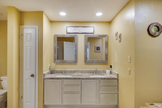 full bath with a textured ceiling, double vanity, a sink, and toilet