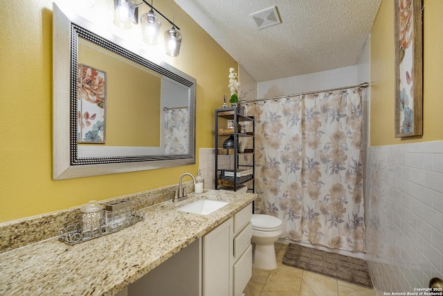 full bath with a textured ceiling, toilet, vanity, visible vents, and tile walls