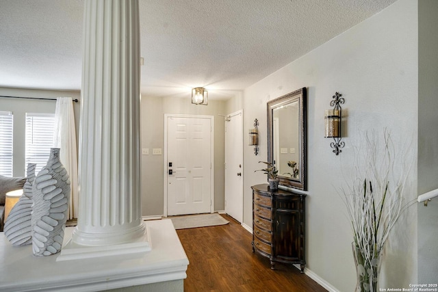 entryway with a textured ceiling, dark wood-type flooring, baseboards, and ornate columns