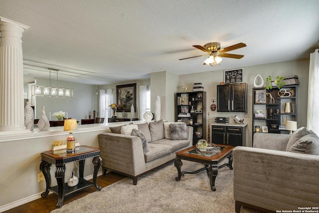 living area featuring ornate columns, a ceiling fan, a textured ceiling, wood finished floors, and baseboards