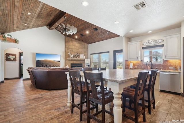 dining room featuring high vaulted ceiling, a stone fireplace, wooden ceiling, light wood-type flooring, and beam ceiling