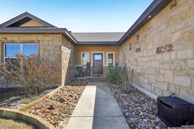 entrance to property featuring stone siding and a shingled roof