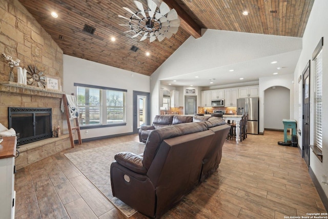 living room featuring high vaulted ceiling, light wood-type flooring, wooden ceiling, and a stone fireplace