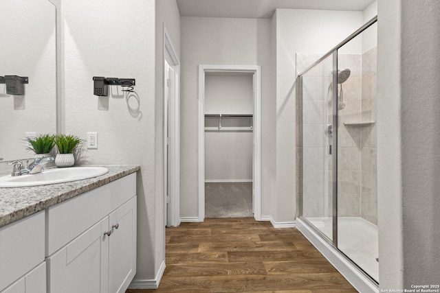 bathroom with a stall shower, a walk in closet, wood finished floors, and vanity