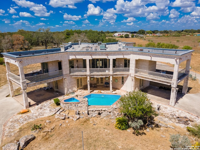 back of house featuring a balcony, a patio area, and an outdoor pool