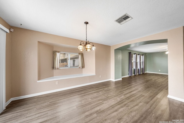 unfurnished room featuring arched walkways, visible vents, an inviting chandelier, wood finished floors, and baseboards