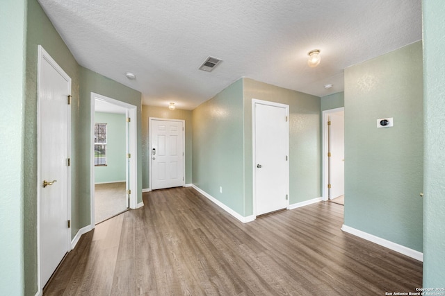 spare room with visible vents, a textured ceiling, baseboards, and wood finished floors