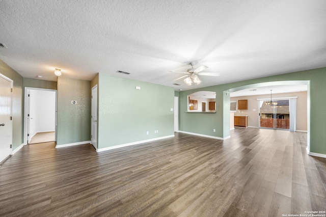 unfurnished living room with dark wood-style floors, baseboards, visible vents, and ceiling fan with notable chandelier