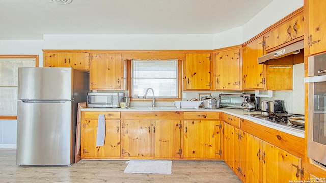 kitchen with light countertops, appliances with stainless steel finishes, a sink, light wood-type flooring, and under cabinet range hood