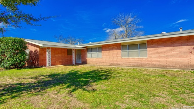 back of house with brick siding and a yard