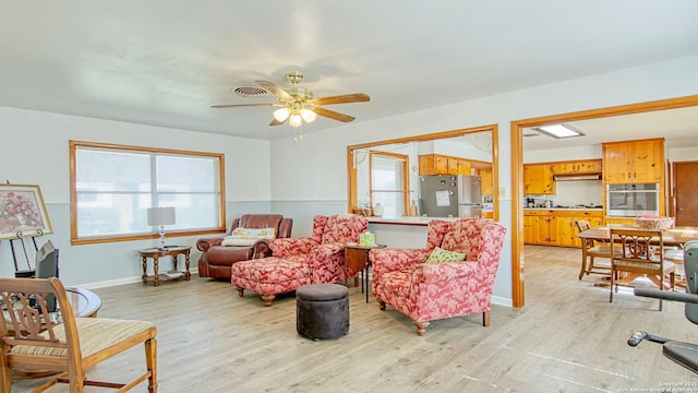 living area with baseboards, light wood-type flooring, visible vents, and a ceiling fan