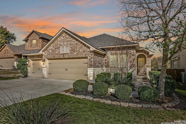 french provincial home with an attached garage, brick siding, concrete driveway, stone siding, and roof with shingles