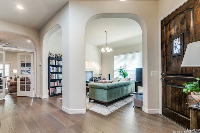 living area featuring a chandelier, arched walkways, wood finished floors, and baseboards